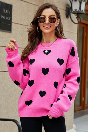 Pink knit sweater with black hearts, crew neck, and balloon sleeves.
