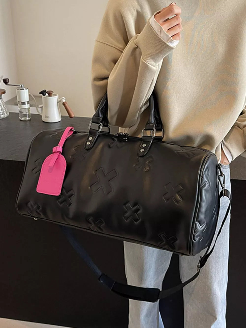 Black embossed cross detail luxury duffel bag with pink tag and shoulder strap
