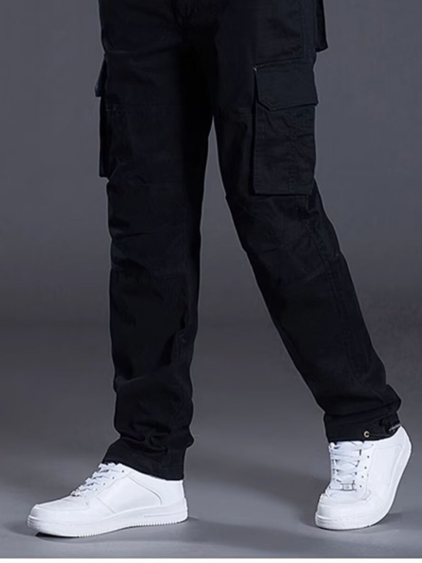 Men's black relaxed fit cargo pants with multiple pockets, styled with white sneakers.