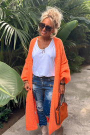 Orange maxi knit cardigan with open front and long sleeves, styled with jeans.