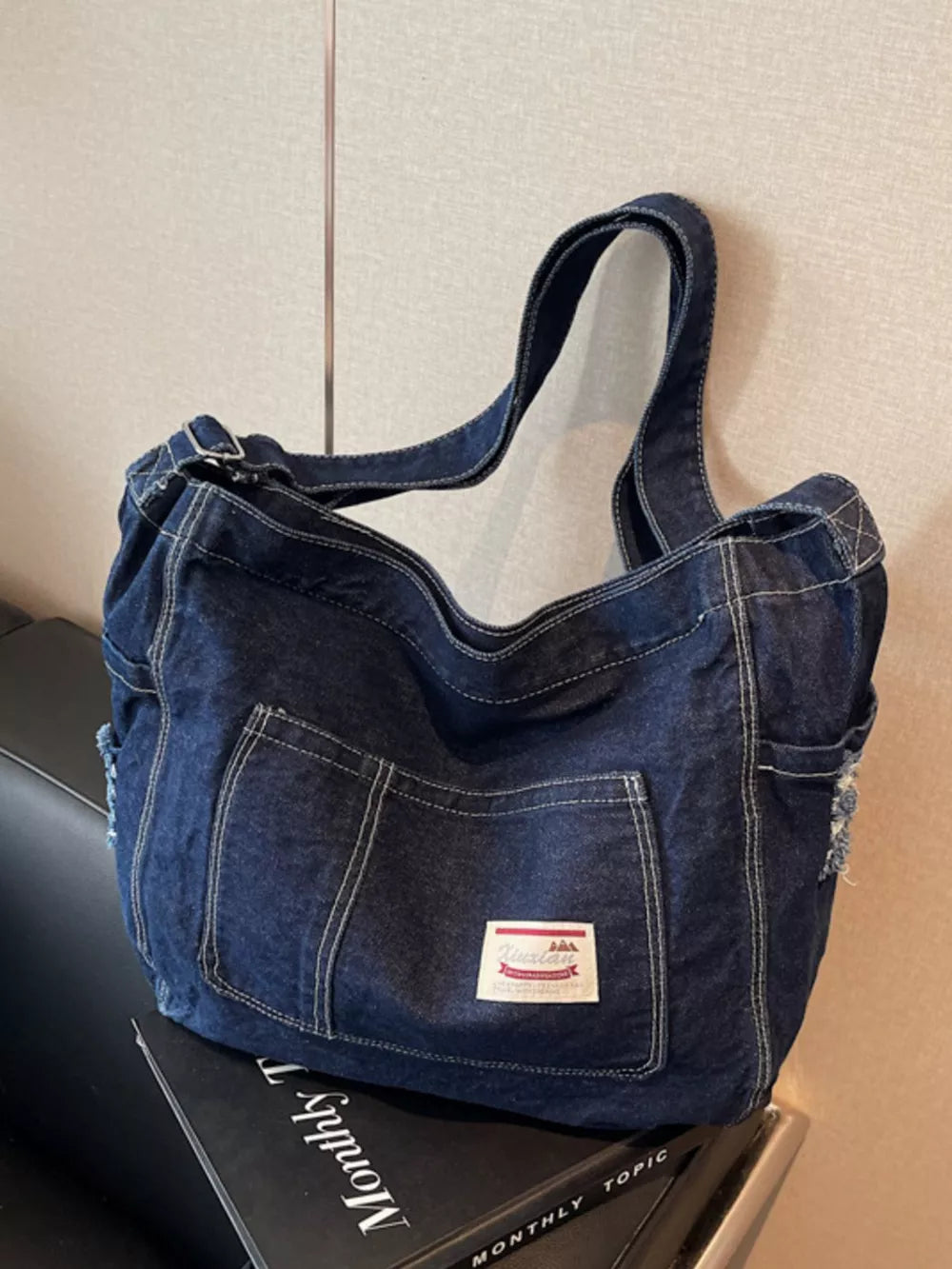 Slouchy denim crossbody bag in blue with contrast stitching and front pockets.