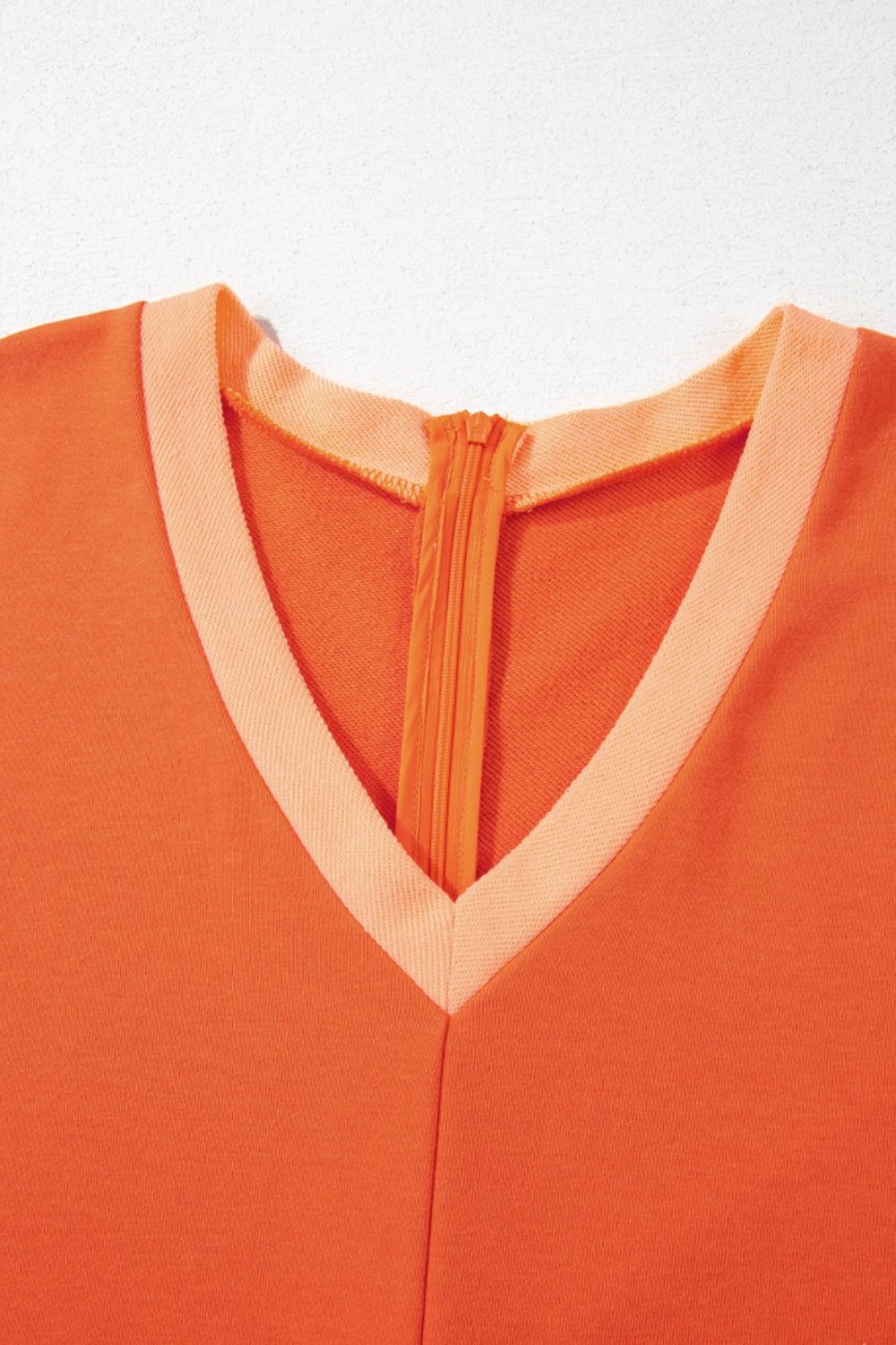 Colorblock V-neck romper in orange with a contrasting trim and zipper detail.