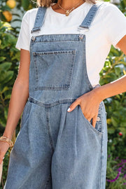 Denim wide-leg jumpsuit with pleated front and buttoned sides, styled with a white tee.