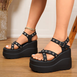Black crisscross wedge sandals with adjustable ankle strap and silver grommets.
