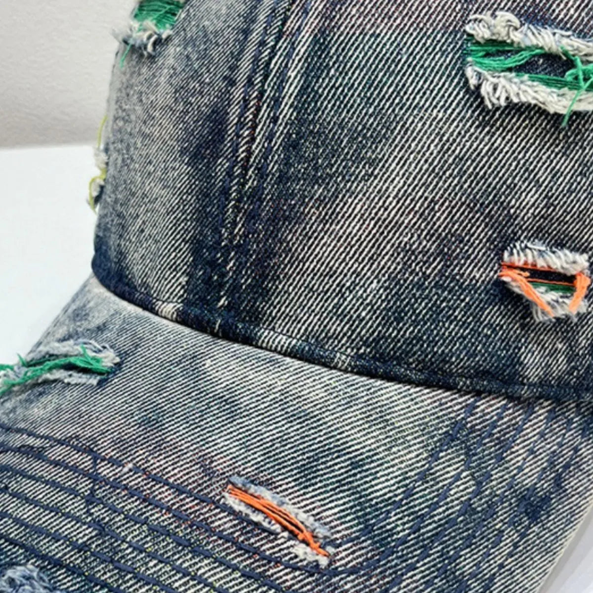Distressed denim baseball cap in light blue with fraying and colorful stitching details.