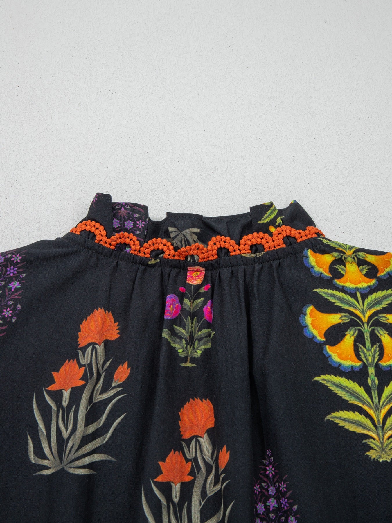 Black cotton maternity shirt with floral print, V-neck, and orange frill detail.