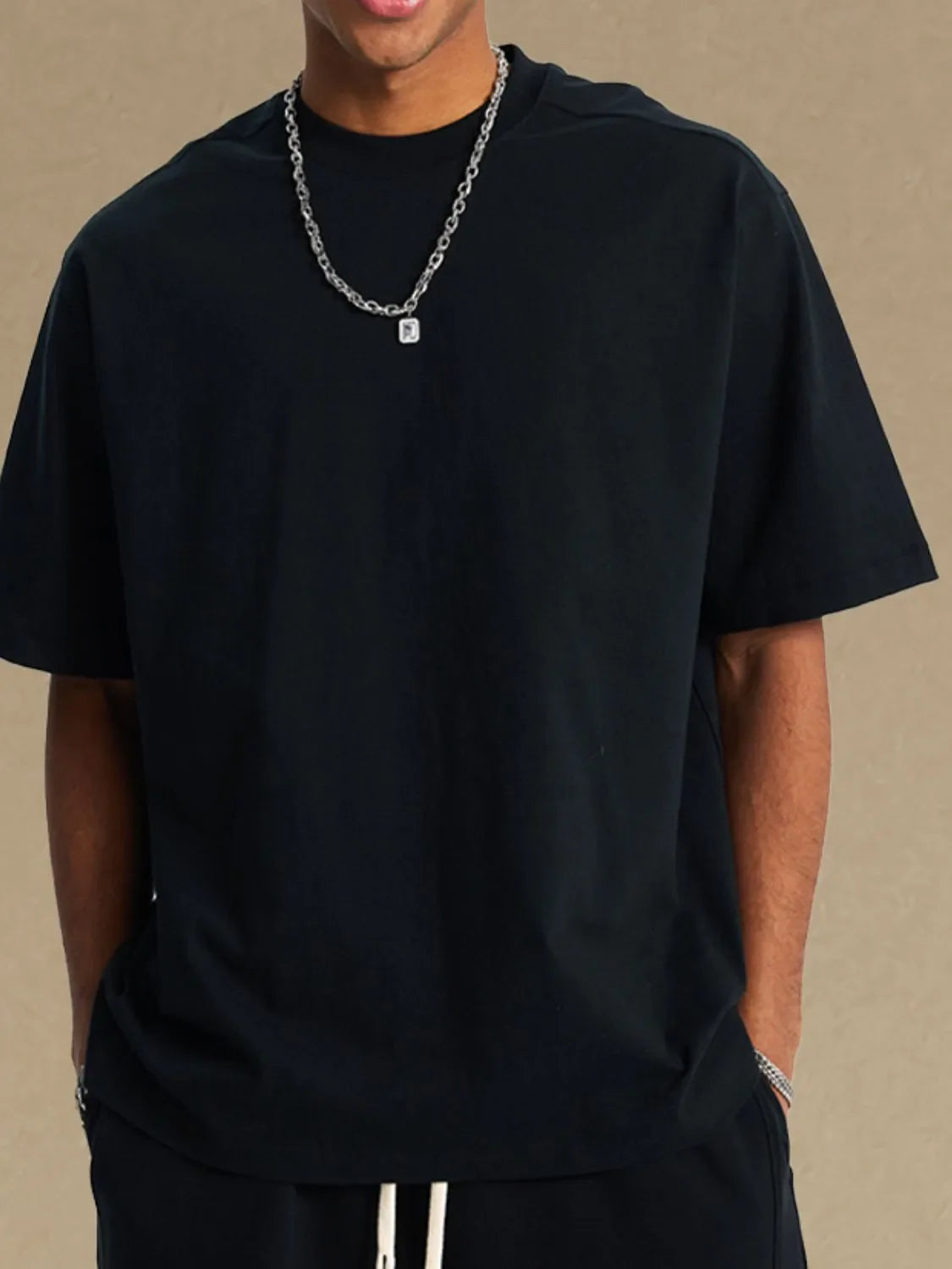 Black boxy cut t-shirt with crew neck and short sleeves, styled with a silver chain necklace.