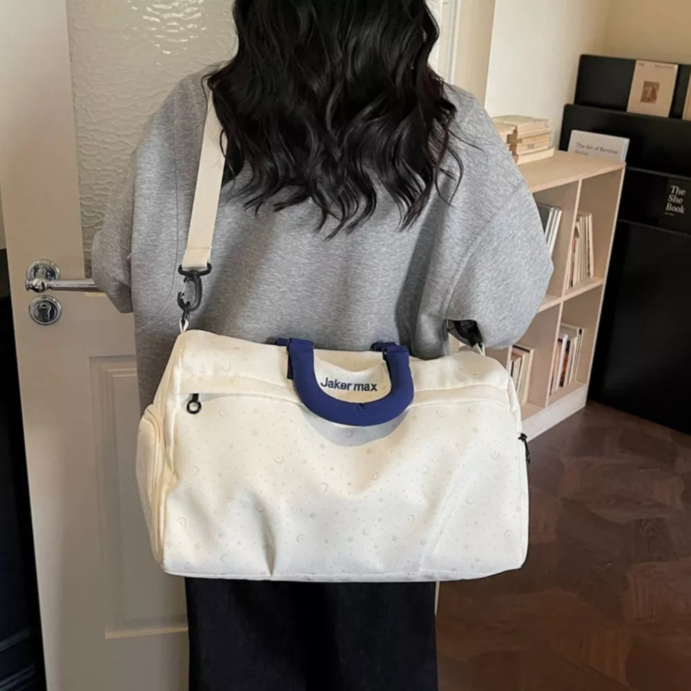 Cream white duffel bag with crescent moon and star pattern, blue handles, and adjustable strap.