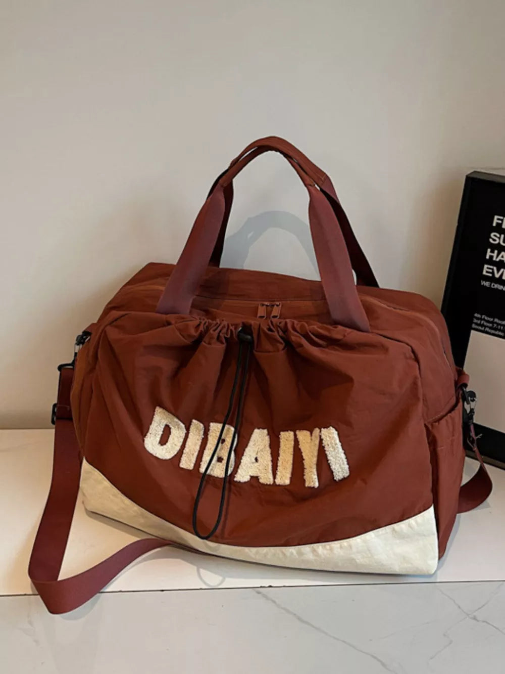 Chic color-blocked travel bag with adjustable strap and embroidered logo detail.