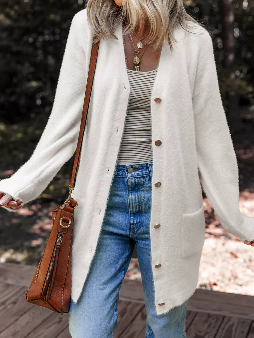 White fuzzy button-front cardigan with pockets and gold buttons, styled with jeans.