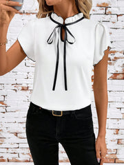 White maternity blouse with frilled tie-neck and black trim, short sleeves.
