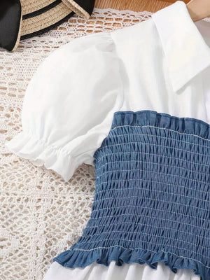 White puff sleeve blouse with blue smocked bodice and ruffled hem.