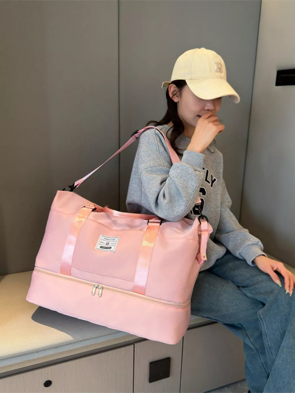 Pink duffel bag with double zipper compartment and pink straps, shown with a woman.