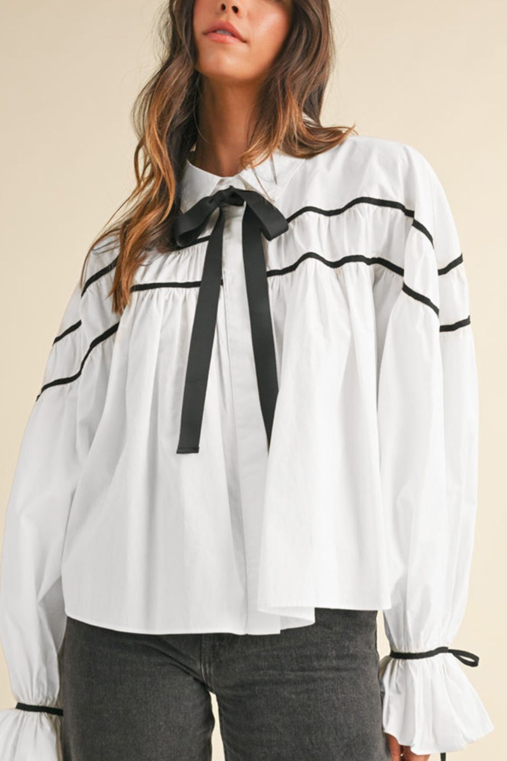 White blouse with black piped trim and bow tie neck, ruffled cuffs.
