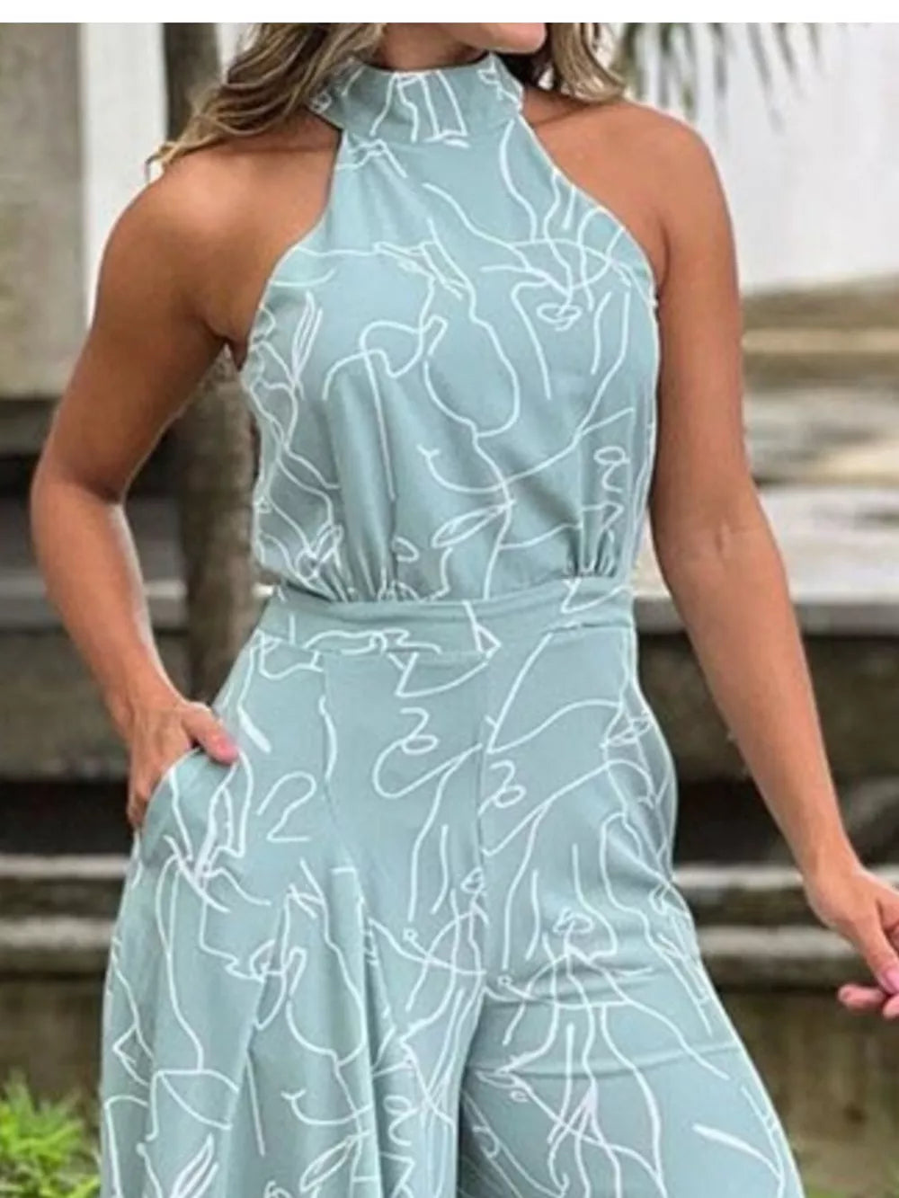 Light blue halter neck romper with abstract white line art print and wide legs.