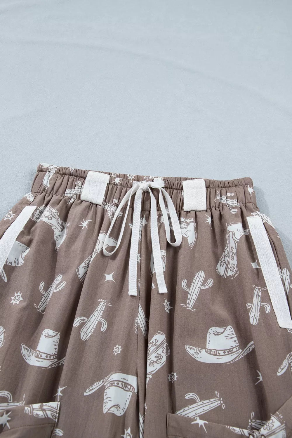 Brown cotton joggers with white western print, drawstring waist, and white side stripe details.