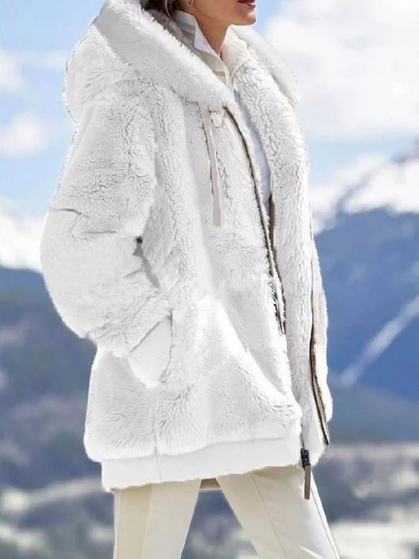 White fuzzy zip-up hoodie with drawstring and pockets, styled with a white shirt and light pants.
