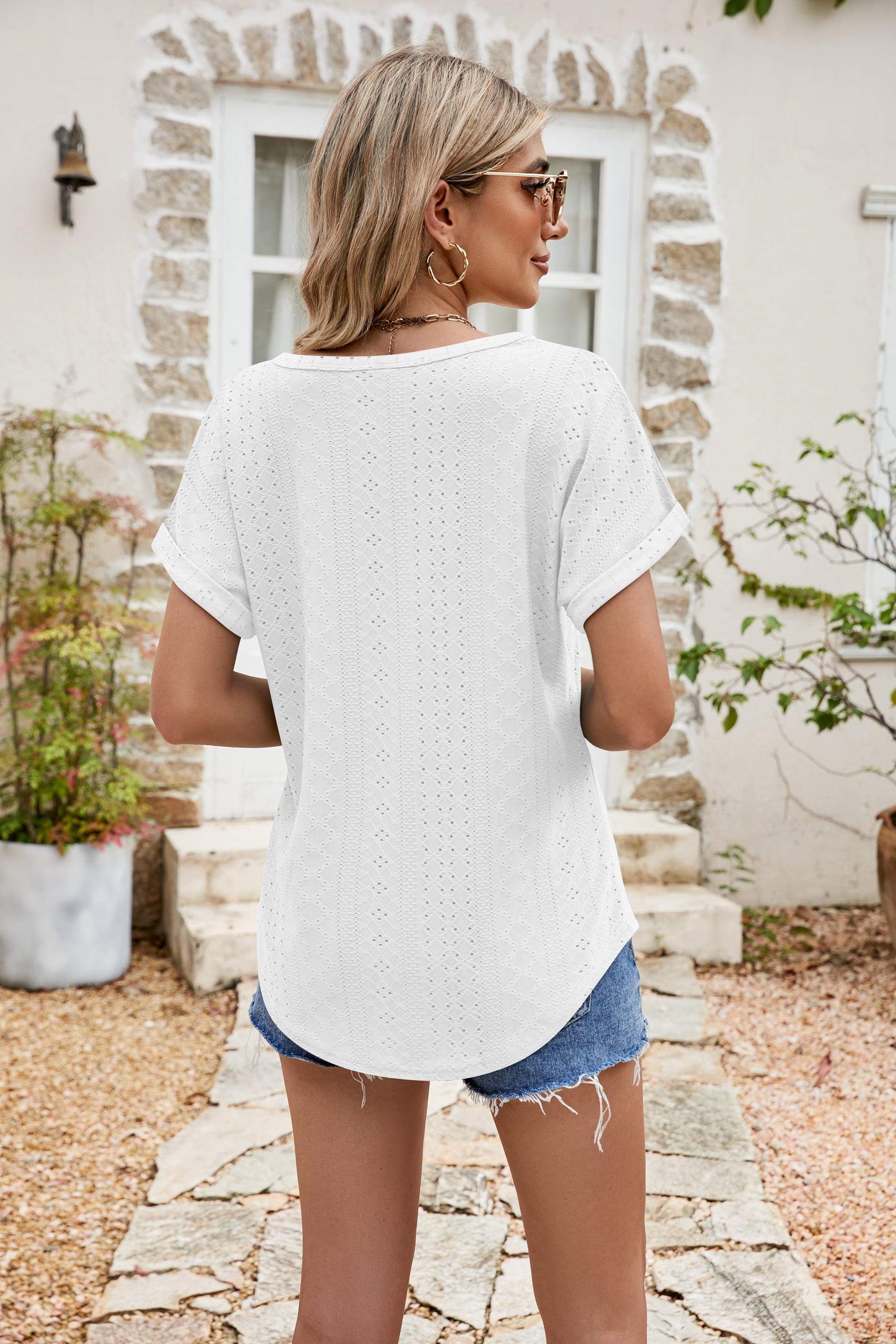 White perforated tee with rolled cuffs and a curved hem, styled with denim shorts.