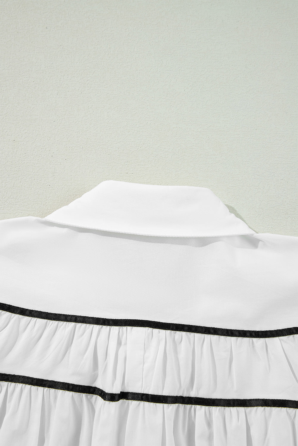 White blouse with black piped trim and ruffled tiers