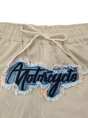 Khaki sweatpants with drawstring and distressed motorcycle graphic patch.