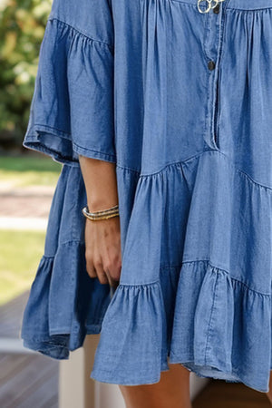 Tiered denim babydoll mini dress in medium blue with bell sleeves and ruffled tiers.