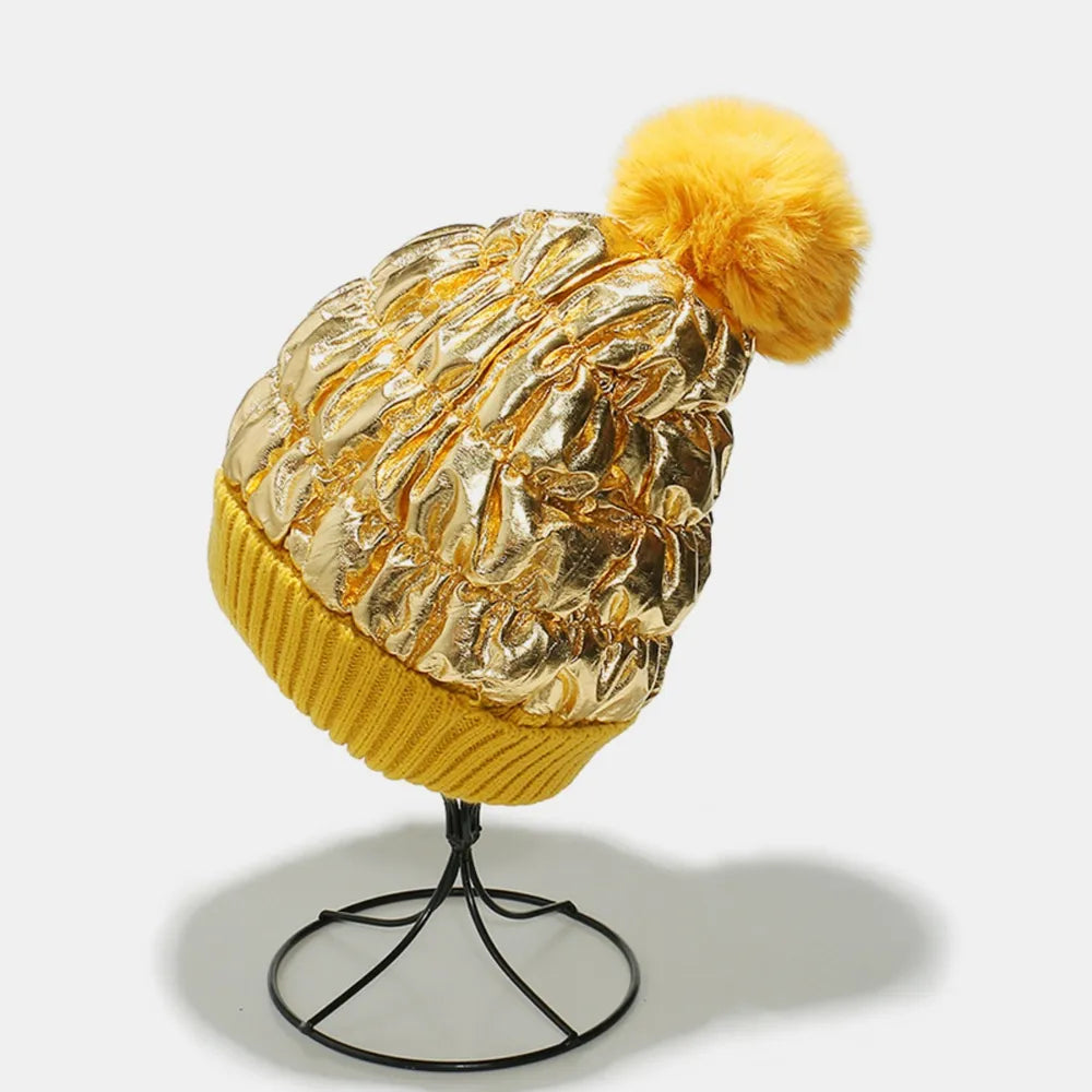 Gold metallic padded beanie with ruched texture and yellow ribbed cuff, topped with a faux fur pom.