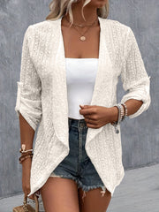White open-weave draped front cardigan with rolled sleeves, styled with a white tube top and denim shorts.