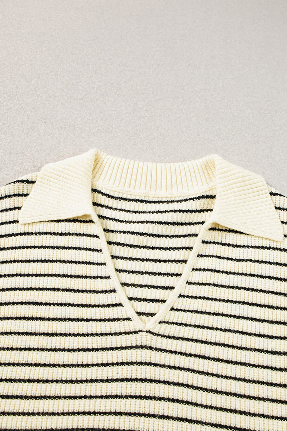 Ivory and black striped knit polo vest with a V-neck and pointed collar.