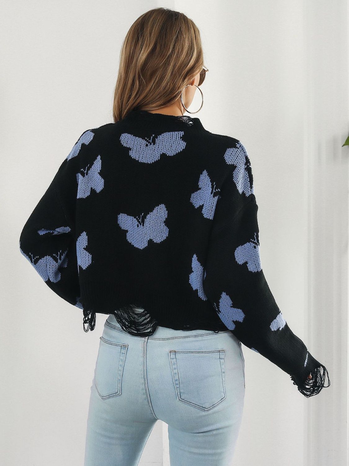 Black cropped knit sweater with distressed butterfly print and frayed hem.