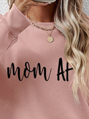 Blush pink crewneck sweatshirt with black "mom At" graphic, crew neck, and ribbed cuffs.