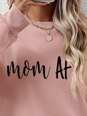 Blush pink crewneck sweatshirt with black "mom At" graphic, crew neck, and ribbed cuffs.