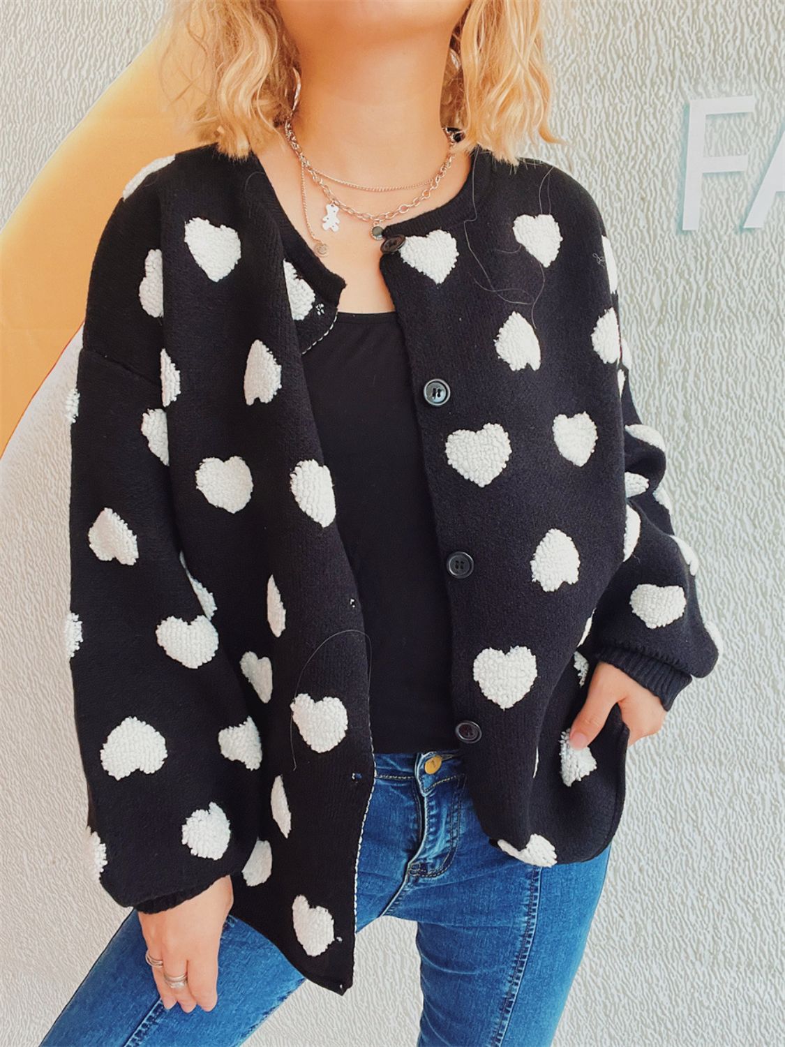 Black acrylic button-down cardigan with textured white heart motif, crew neck, and long sleeves.