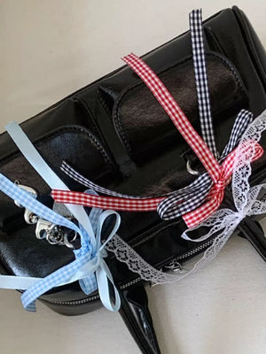Black patent shoulder bag with red, blue, and black gingham ribbon embellishments.