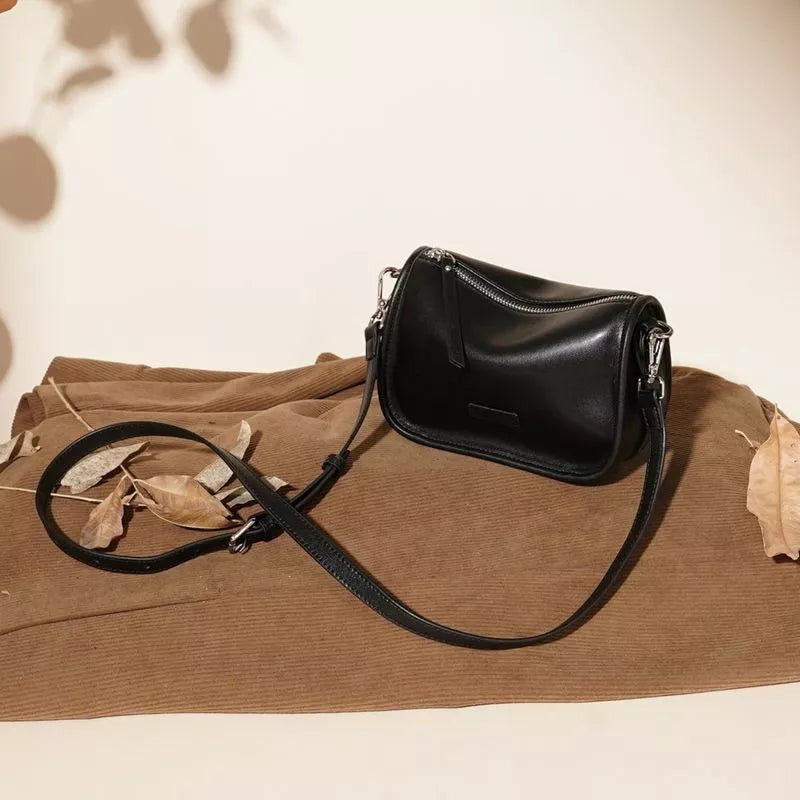 Sleek black leather crossbody bag with adjustable strap and silver zipper detail.