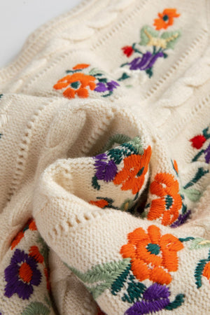 Beige cable knit vest with floral embroidery and cable knit texture detail.