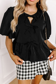 Black peplum blouse with puff sleeves, keyhole neckline, and bow details.