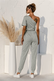 Gray asymmetric sweat jumpsuit with drawstring waist and cuffed jogger pants.