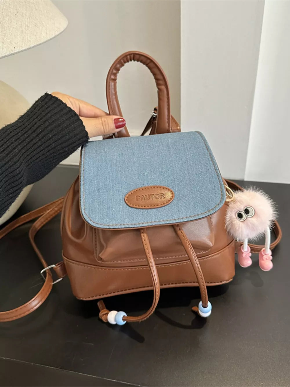 Brown leather mini backpack with denim flap and beaded drawstring detail.