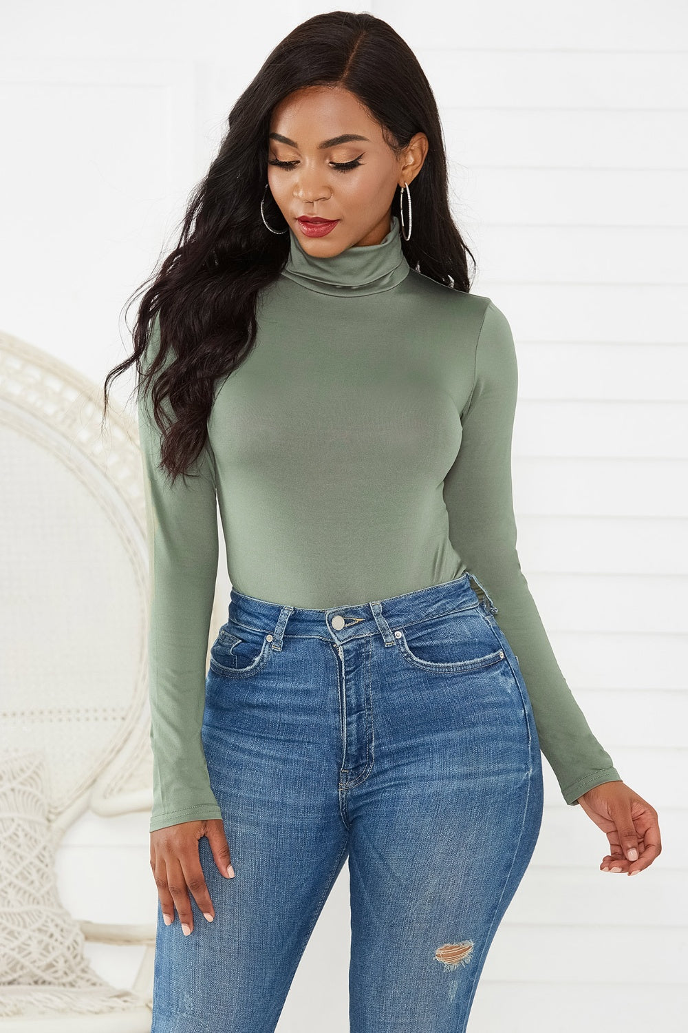 Sage green turtleneck bodysuit with long sleeves, paired with distressed denim jeans.