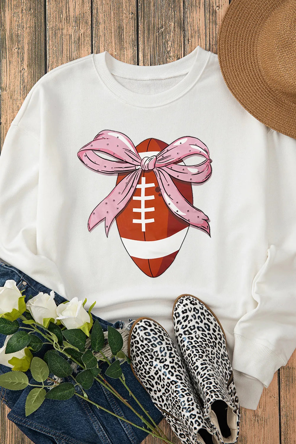 White crewneck sweatshirt with a football graphic adorned with a pink polka dot bow.