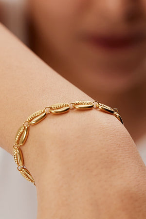 Gold cowrie shell bracelet with textured detailing on a wrist.