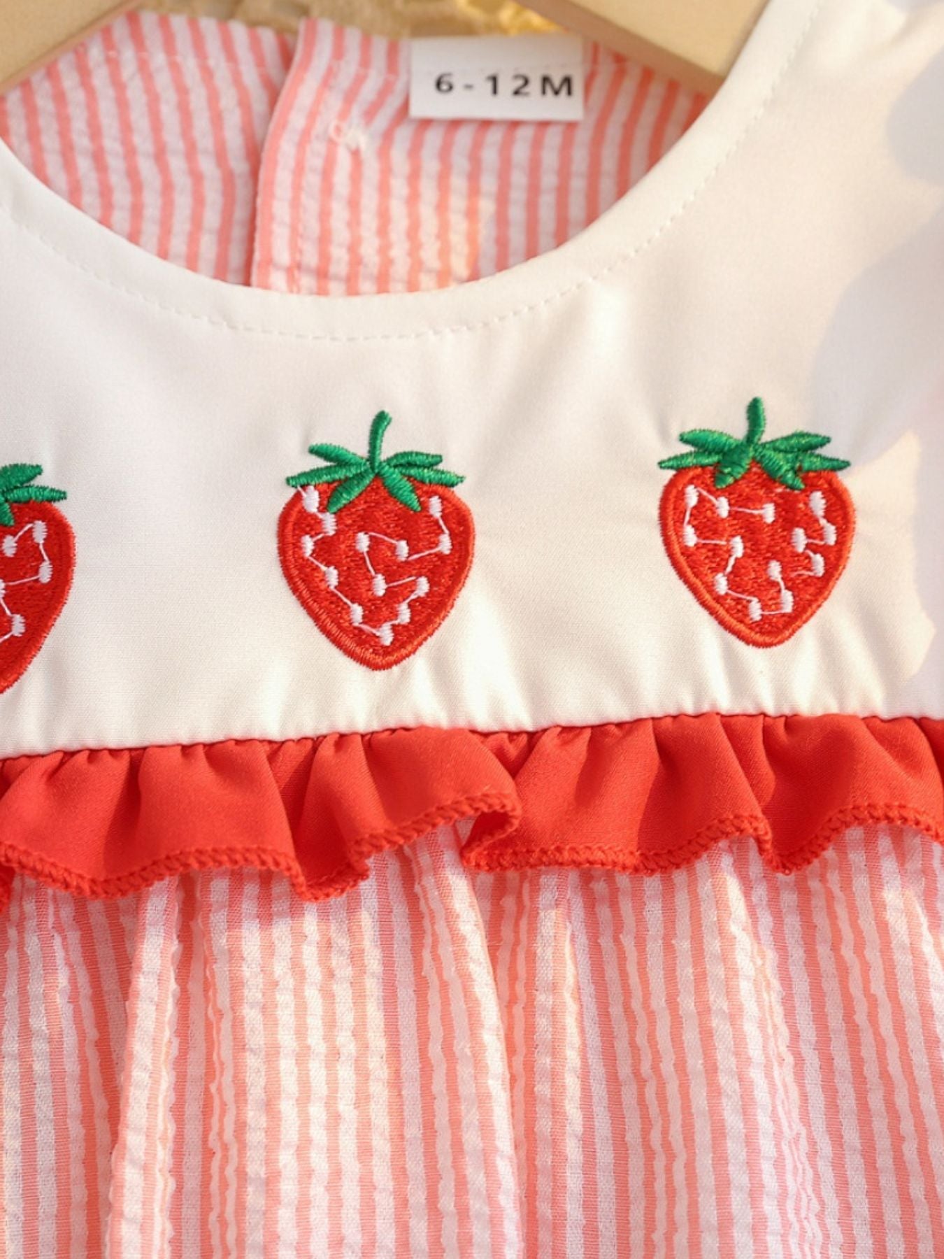 Baby dress with embroidered strawberries and red ruffle trim on striped cotton fabric.