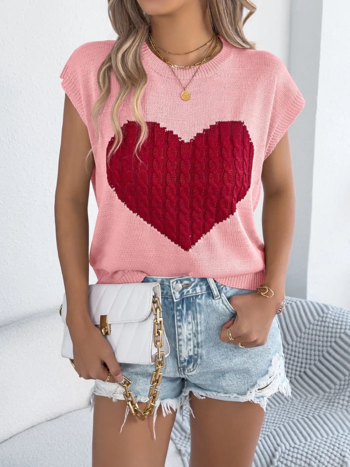 Blush pink cable knit sweater vest with a red cable knit heart graphic and crew neck.