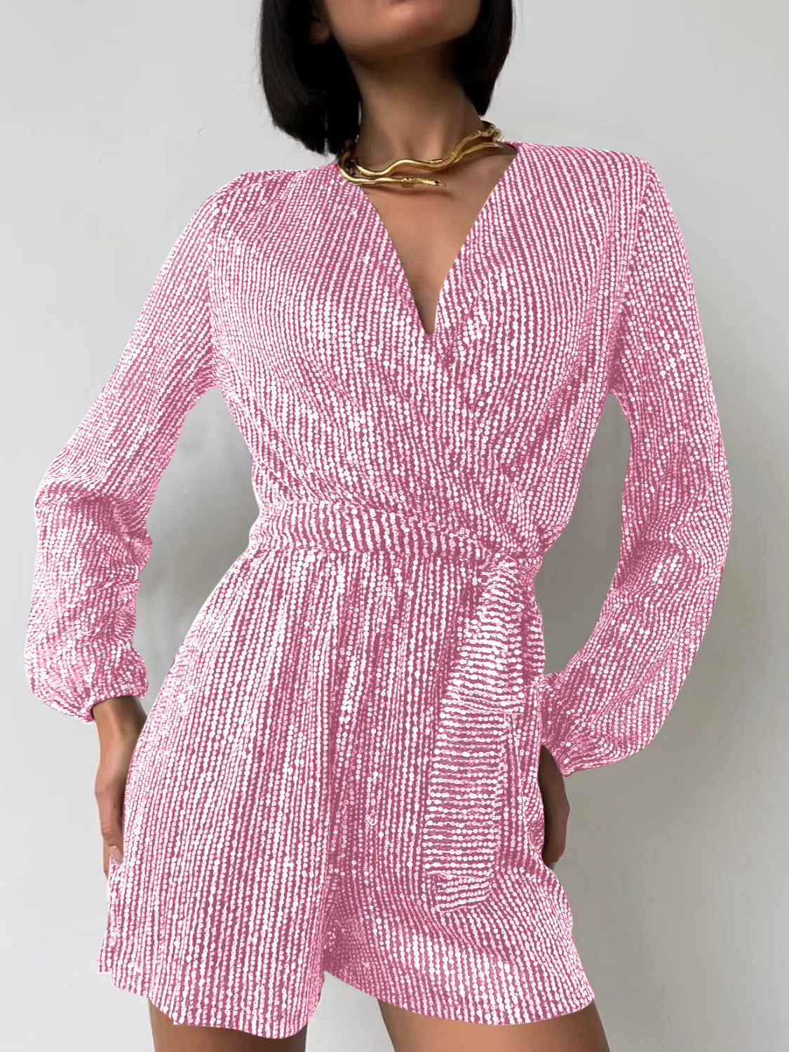 Pink sequin wrap romper with blouson sleeves and a V-neckline.
