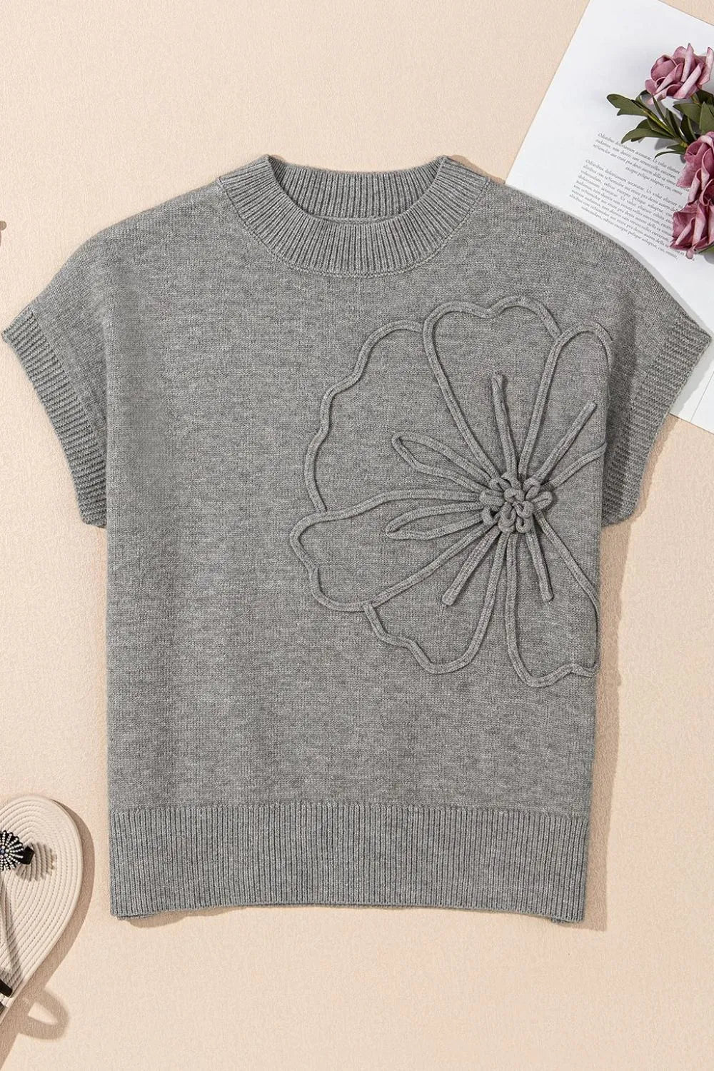 Gray knit blouse with short sleeves and a large embroidered flower detail on the chest.