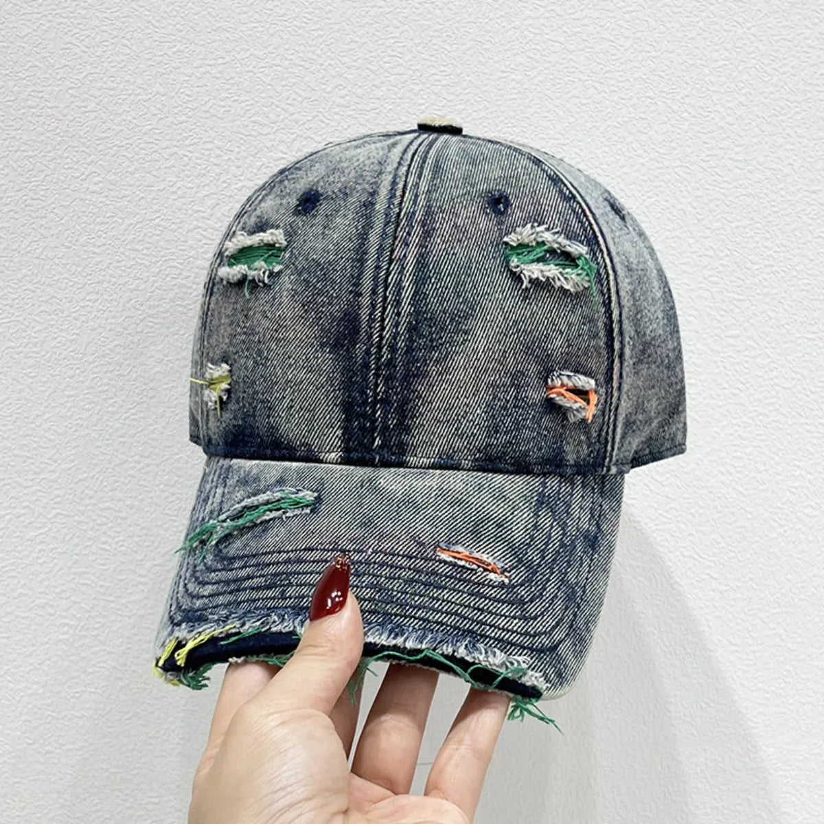 Distressed denim baseball cap with fraying and colorful stitching details.