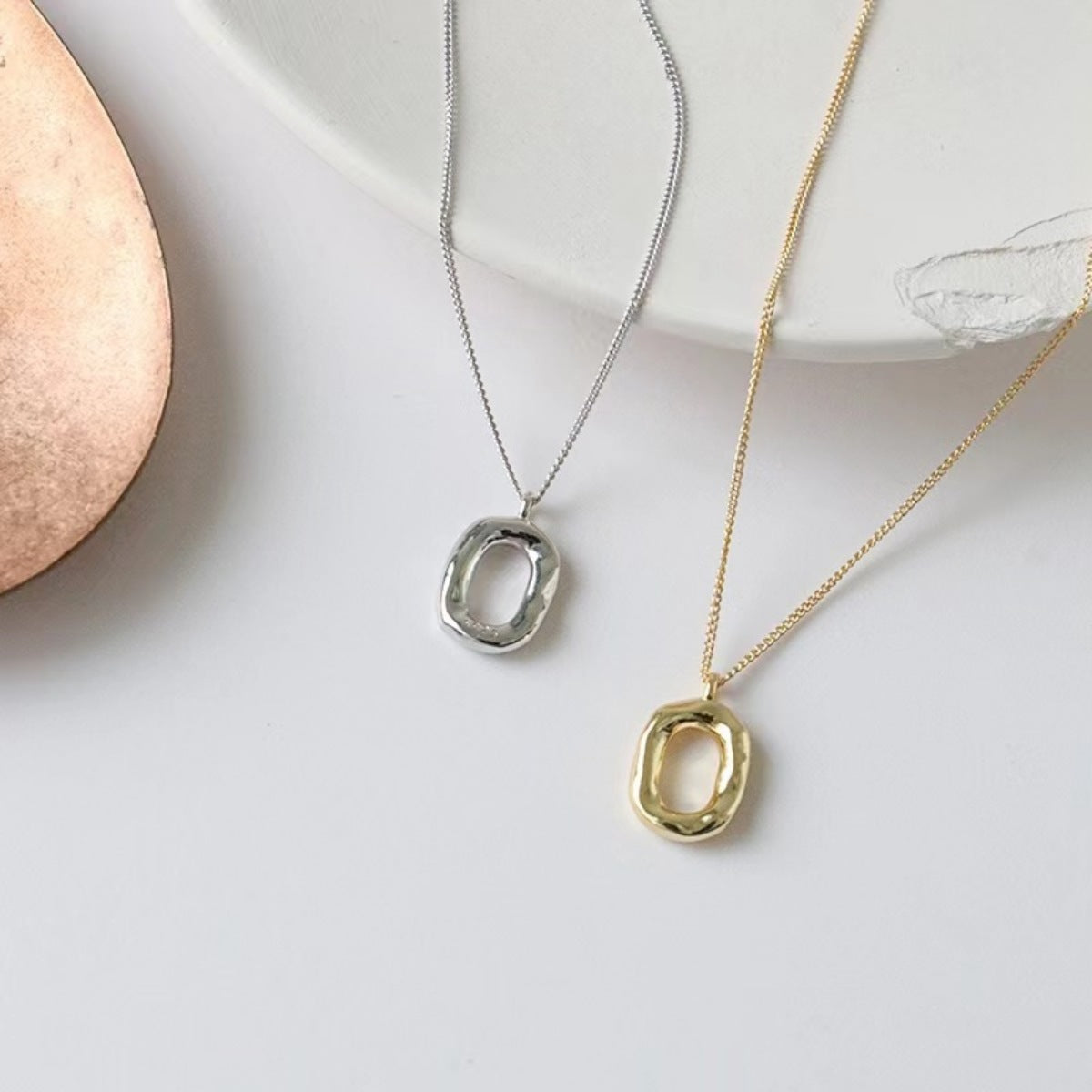 Geometric pendant necklaces in silver and gold with abstract oval pendants.
