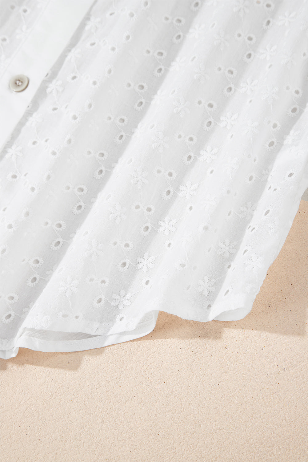 White embroidered eyelet blouse with poet sleeves and a button detail.