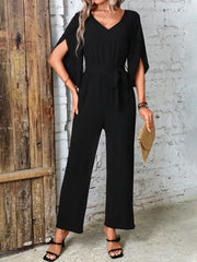 Black cape sleeve wrap jumpsuit with tie waist and wide leg pants.