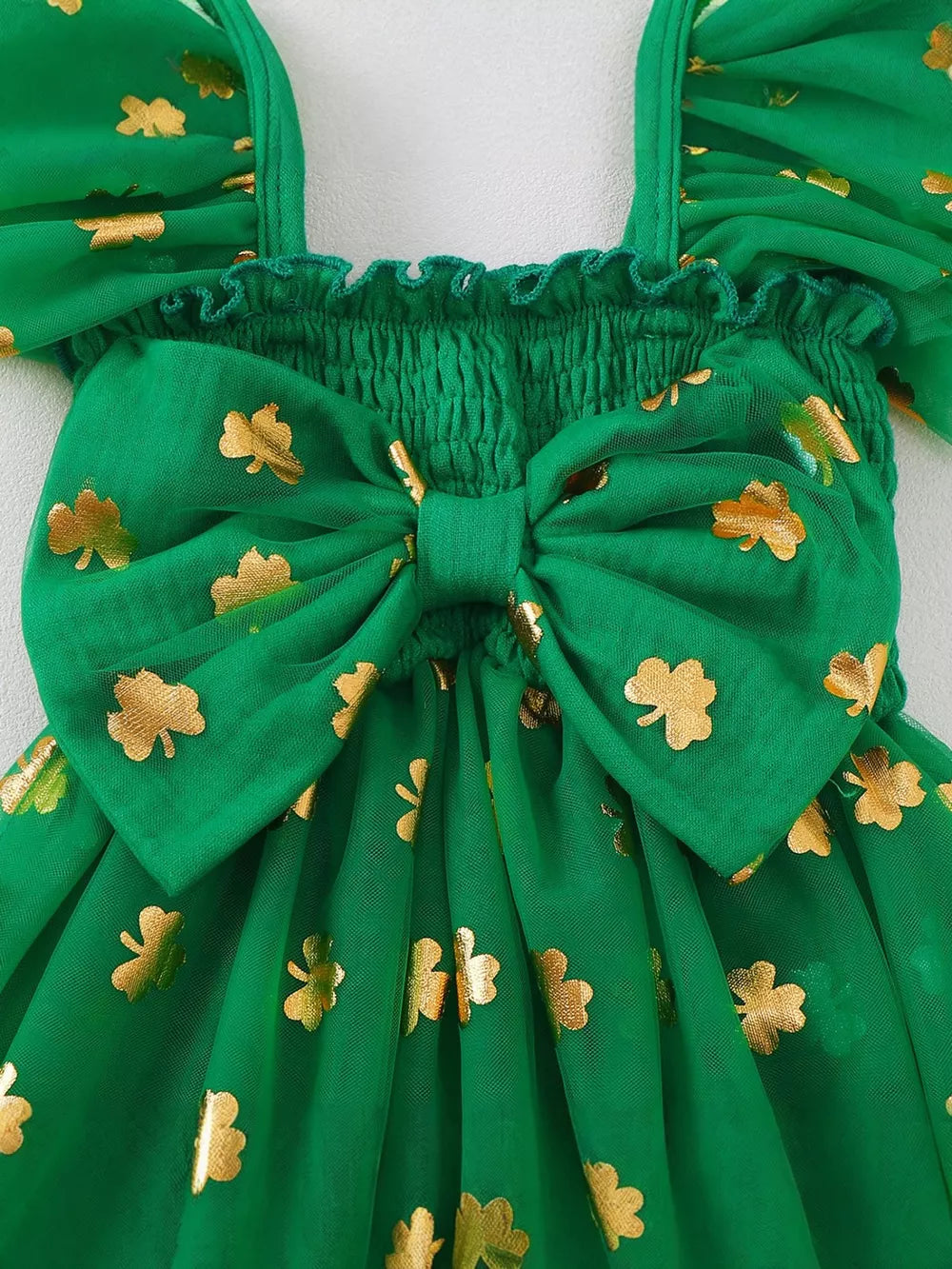 Green tulle baby dress with smocked bodice, gold shamrock print, and large bow detail.
